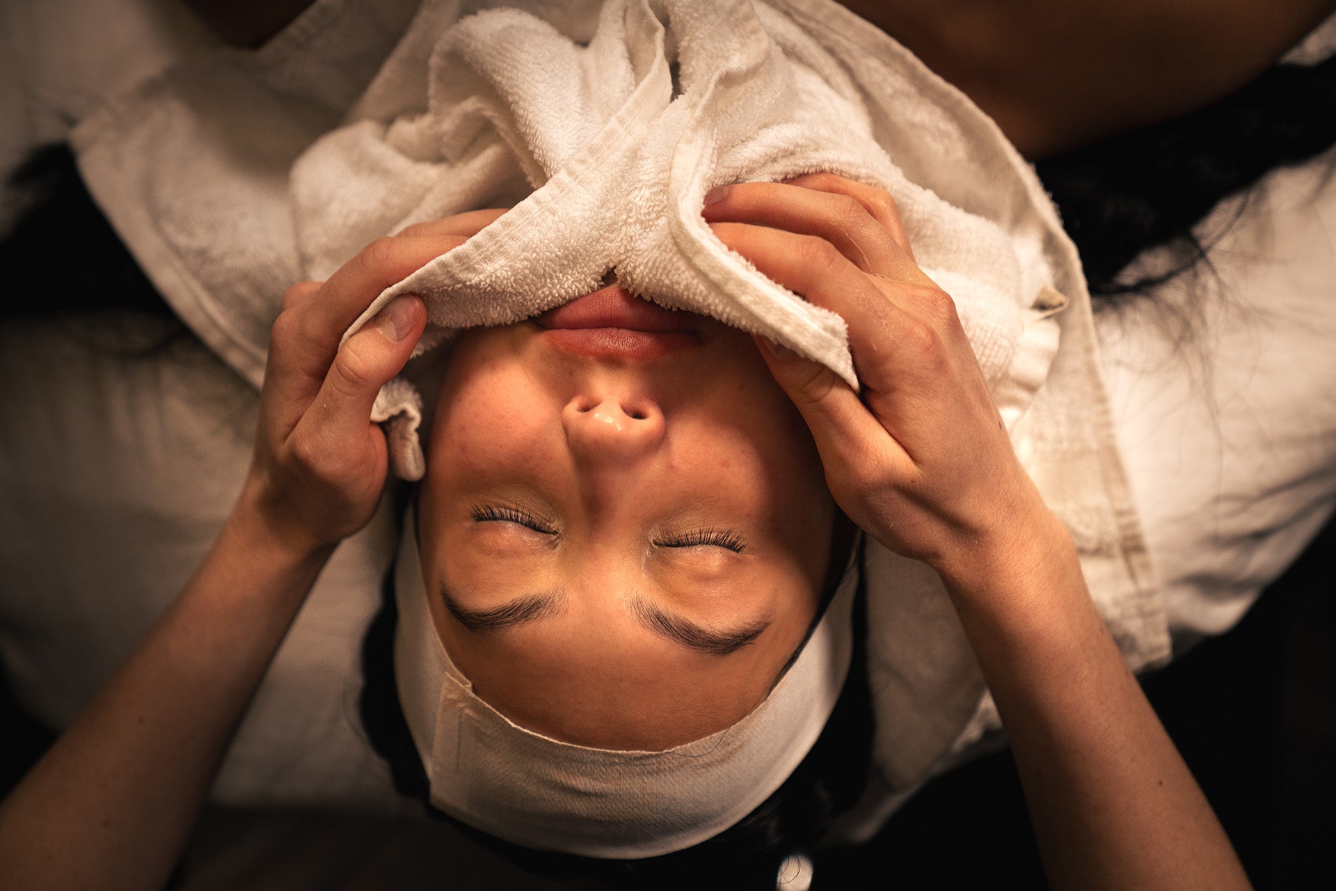 Person receiving a head massage with a towel on their face